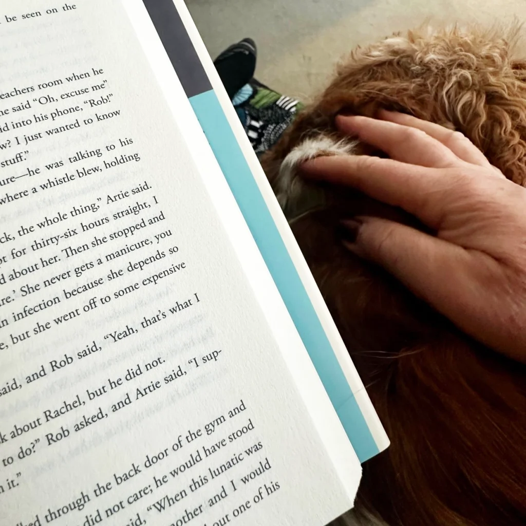 Angelina Eynon reading a novel while her dog Alfie rests beside her